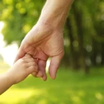Adult holding child's hand in green field